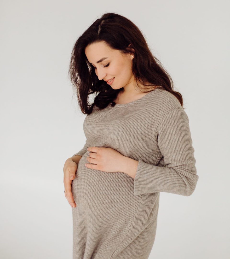 Beautiful young pregnant woman posing in studio in dress